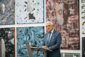Ein Redner am Pult vor einer Wand voller Kunstwerke