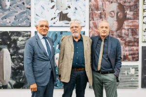 Drei Herren stehen vor eine Wand mit Kunstwerken